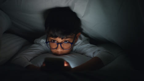 Close-Up-Of-Young-Boy-In-Bedroom-At-Home-Using-Mobile-Phone-To-Text-Message-Under-Covers-Or-Duvet-At-Night-6